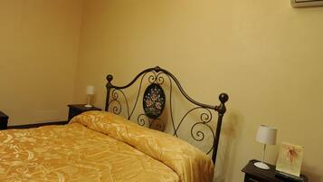 Un dormitorio con una cama, una mesita de noche, una lámpara y un aire acondicionado de pared.