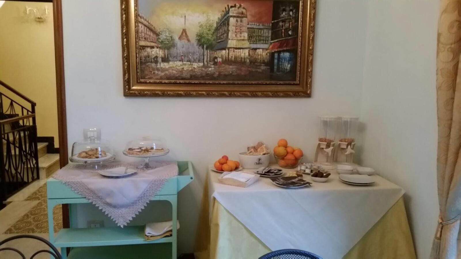Een eetgedeelte met een tafel gedekt voor het ontbijt, inclusief fruit en gebak, en een schilderij erboven.