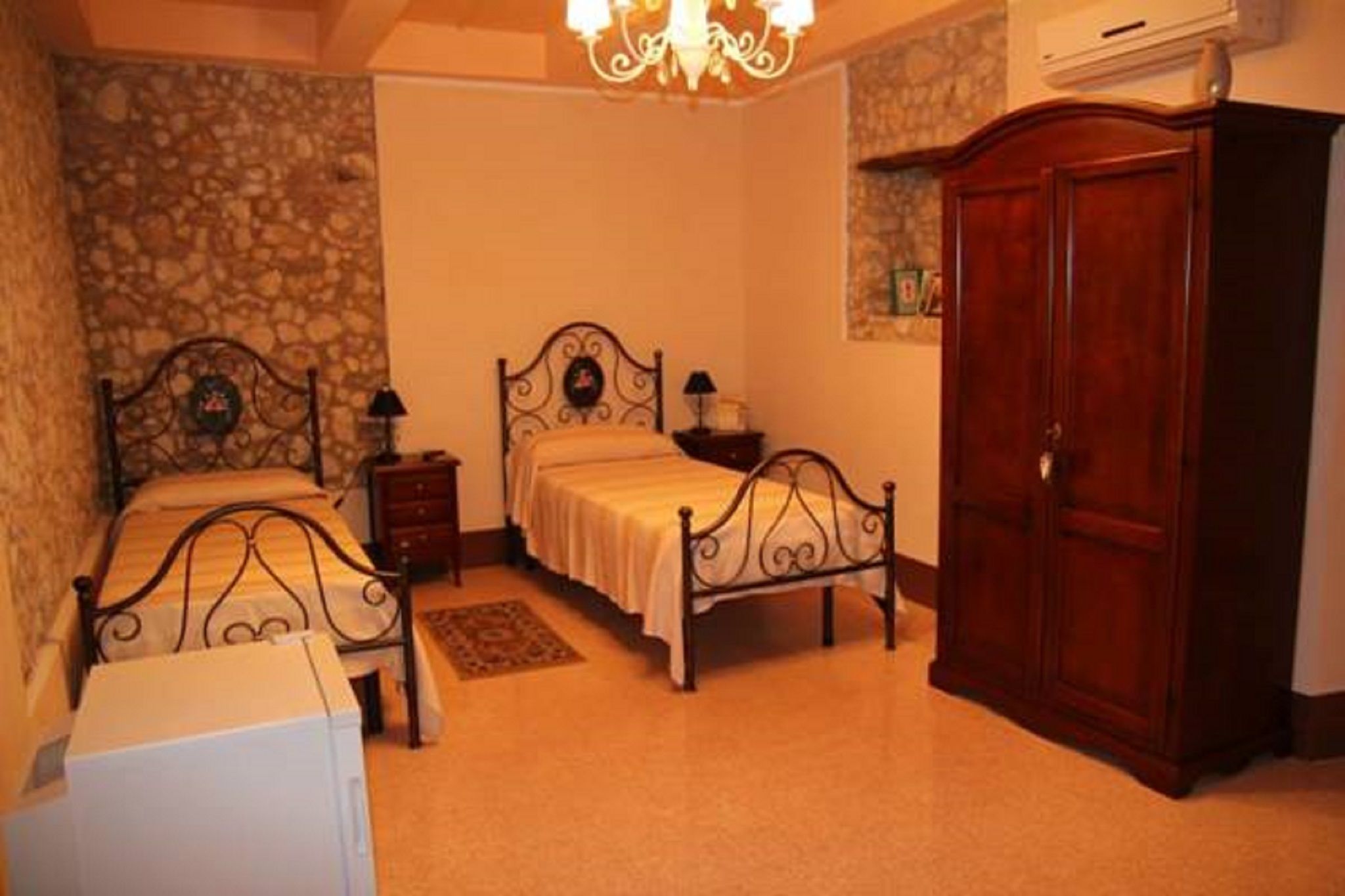 A bedroom with two beds, a wardrobe, a chandelier, and a stone wall.