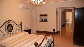 Een slaapkamer met een bed, nachtkastje, wandplank en een deur naar een andere kamer.