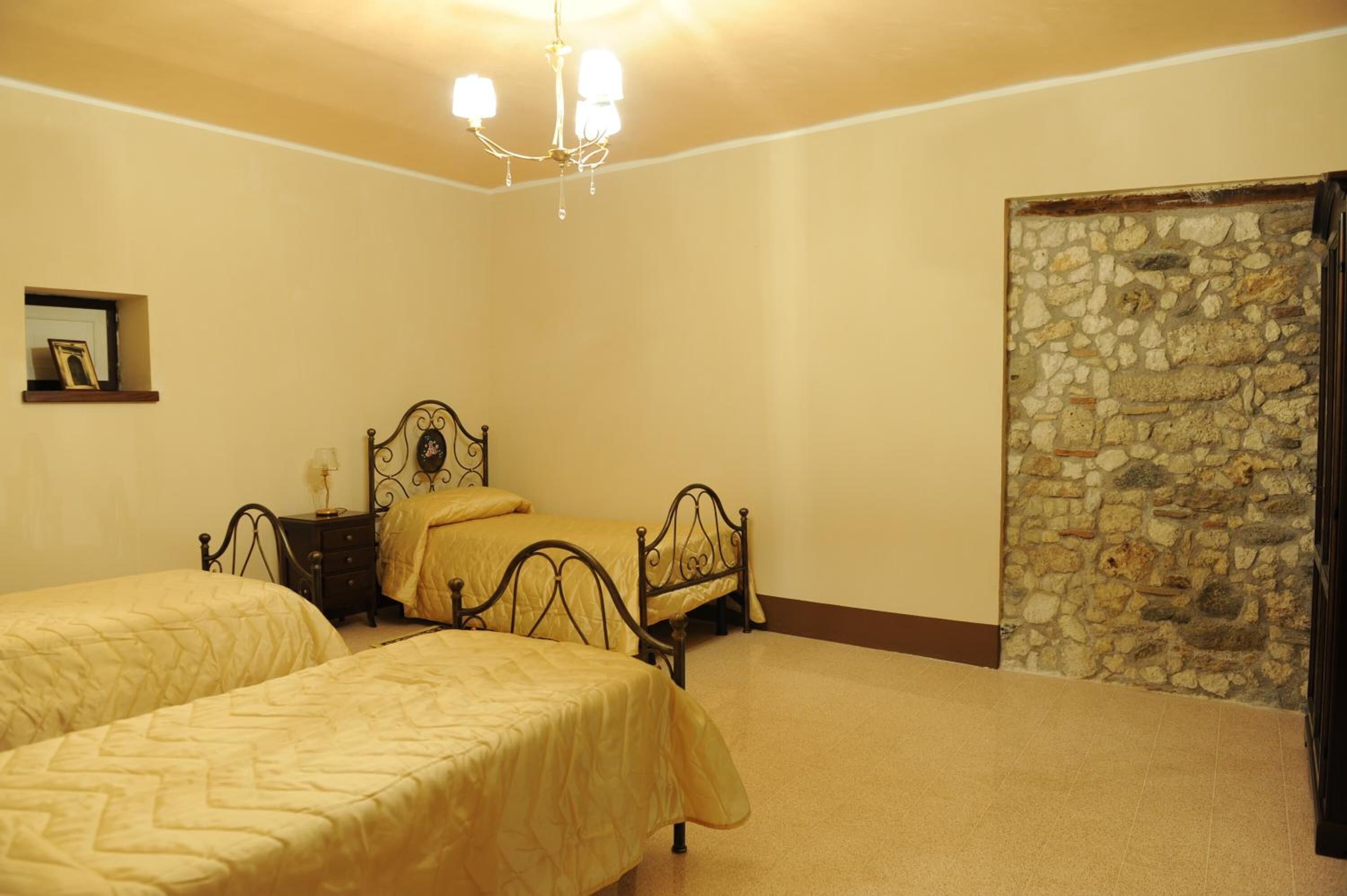 A room with two beds, a chandelier, a stone wall, and a small shelf with a picture frame.
