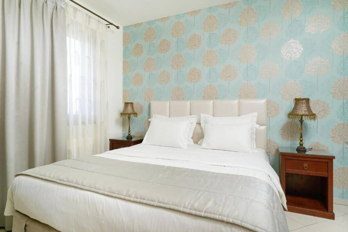 Um quarto com uma cama, cortinas, uma mesa de cabeceira e uma luminária.
