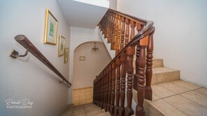 A wooden staircase with a handrail, a landing with a wall-mounted light fixture, and framed pictures on the wall. - Henry's GuestHouse - Hostel (San Juan)