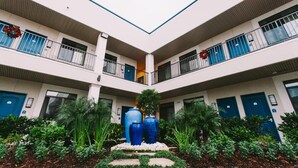 A multi-story building with a central courtyard featuring large blue vases, surrounded by greenery and white pillars. - Palace Inn City Center (Houston)