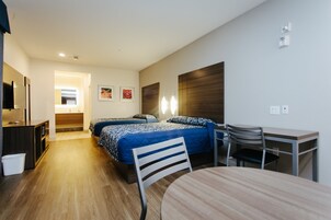 A hotel room with two beds, a desk, a chair, a TV, and a small table.