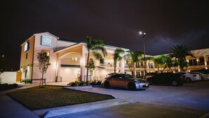 A hotel with a modern design, featuring a central courtyard with palm trees and a parking area with several cars. - Palace Inn City Center (Houston)