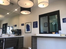 Une salle de bain moderne avec un grand miroir, une machine à café et un lavabo. On y trouve des luminaires au plafond et un tableau encadré accroché au mur.