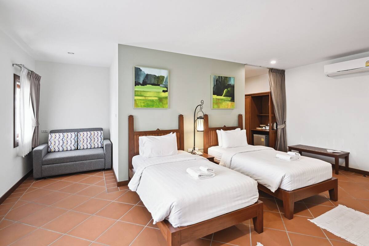 A hotel room with two beds, a sofa, a desk, and artwork on the walls.