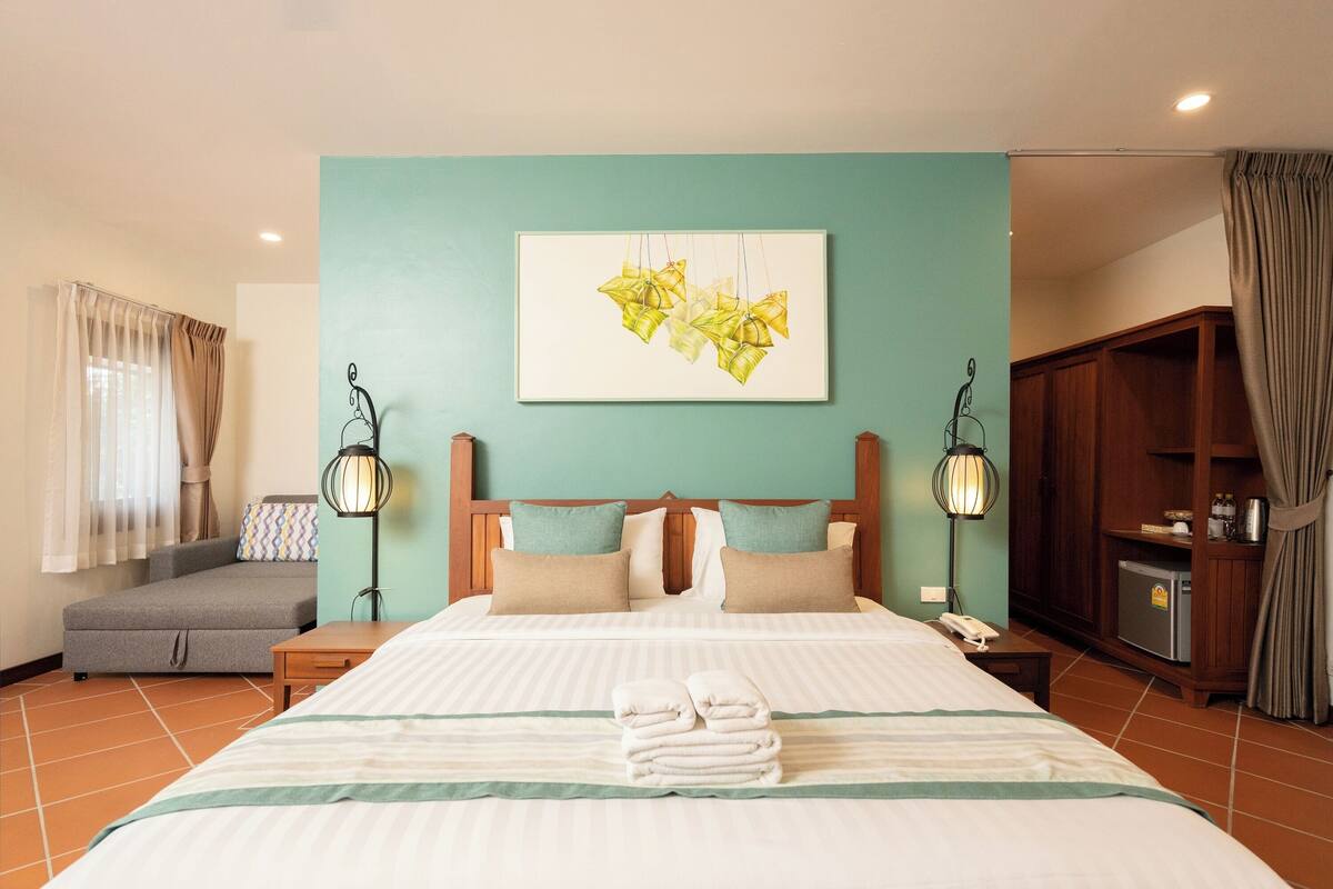 A hotel room with a large bed, a sofa, a desk, and a wardrobe.