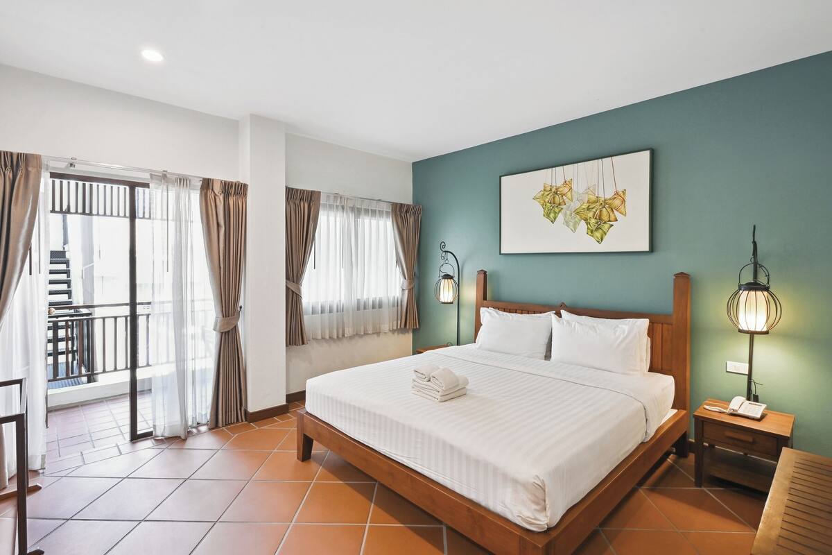 A hotel room with a large bed, a nightstand with a lamp, a painting on the wall, and a view of a balcony.