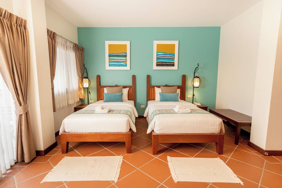 A twin room with two beds, a bench, and artwork on the wall.