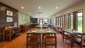 A spacious dining area with wooden tables and chairs, a buffet counter, and large windows offering views of the outdoors. - Villa Sanpakoi (Chiang Mai)