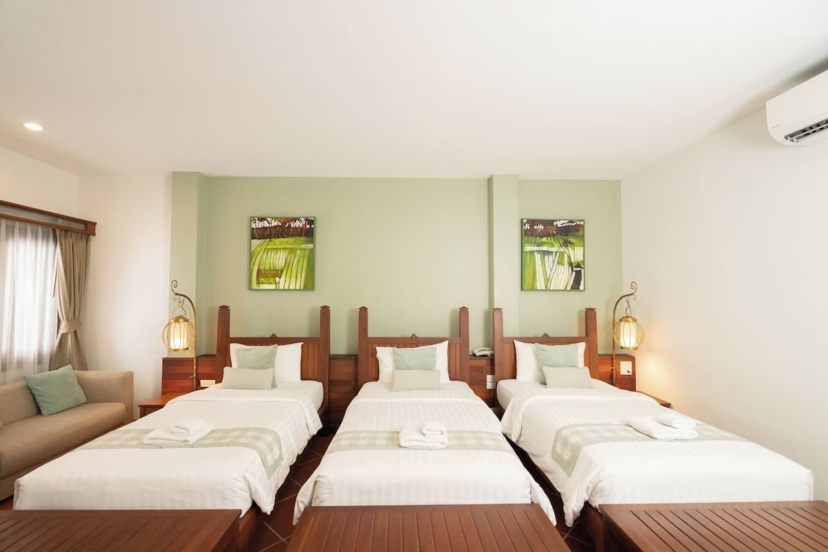 A hotel room with three single beds, a sofa, and a wooden table.