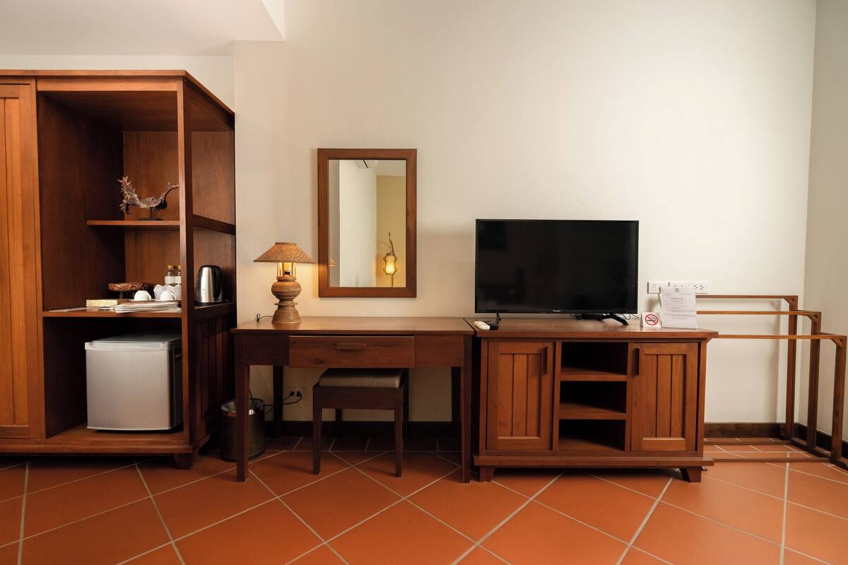 A compact room with a wooden desk, a television, a mirror, and a small refrigerator.