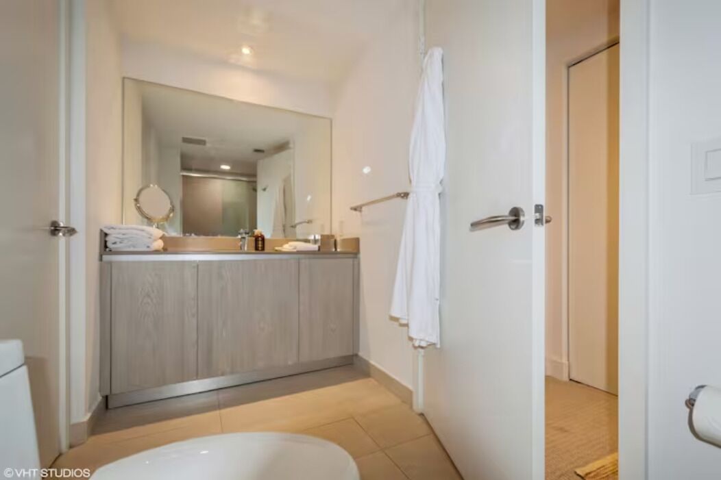 Un baño moderno con tocador de madera, un espejo grande y una toalla blanca colgada en la pared.