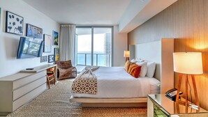 A modern hotel room with a large bed, a desk with a computer, a chair, a lamp, and a view of the city. - Lyfe Residence Building - Private apts over the beach (Hollywood)