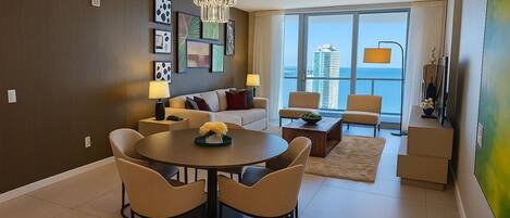 A modern living room with a dining area, large windows, and a view of the city.