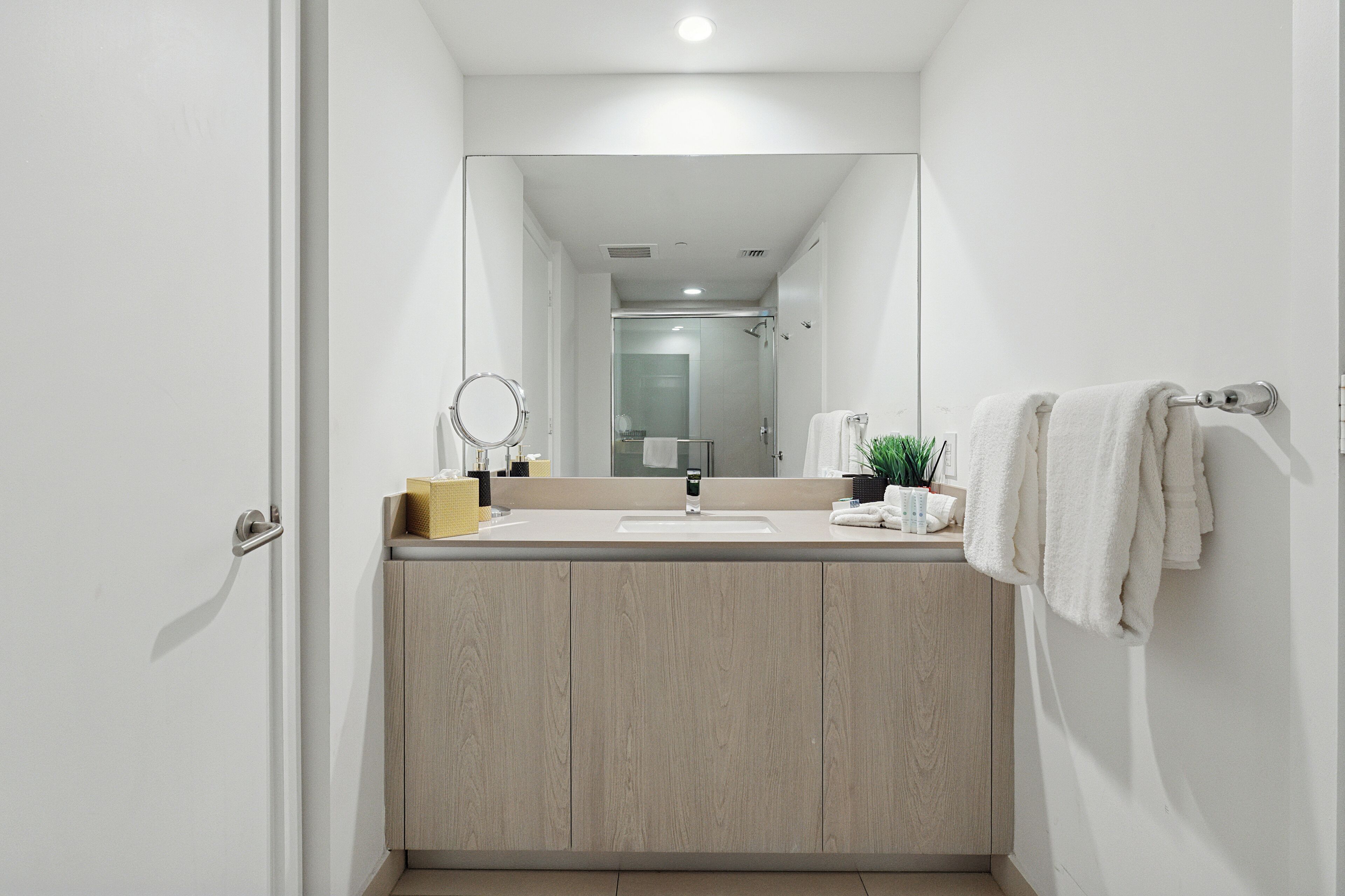 Un baño moderno con tocador de madera, espejo, lavamanos y perchero para toallas.