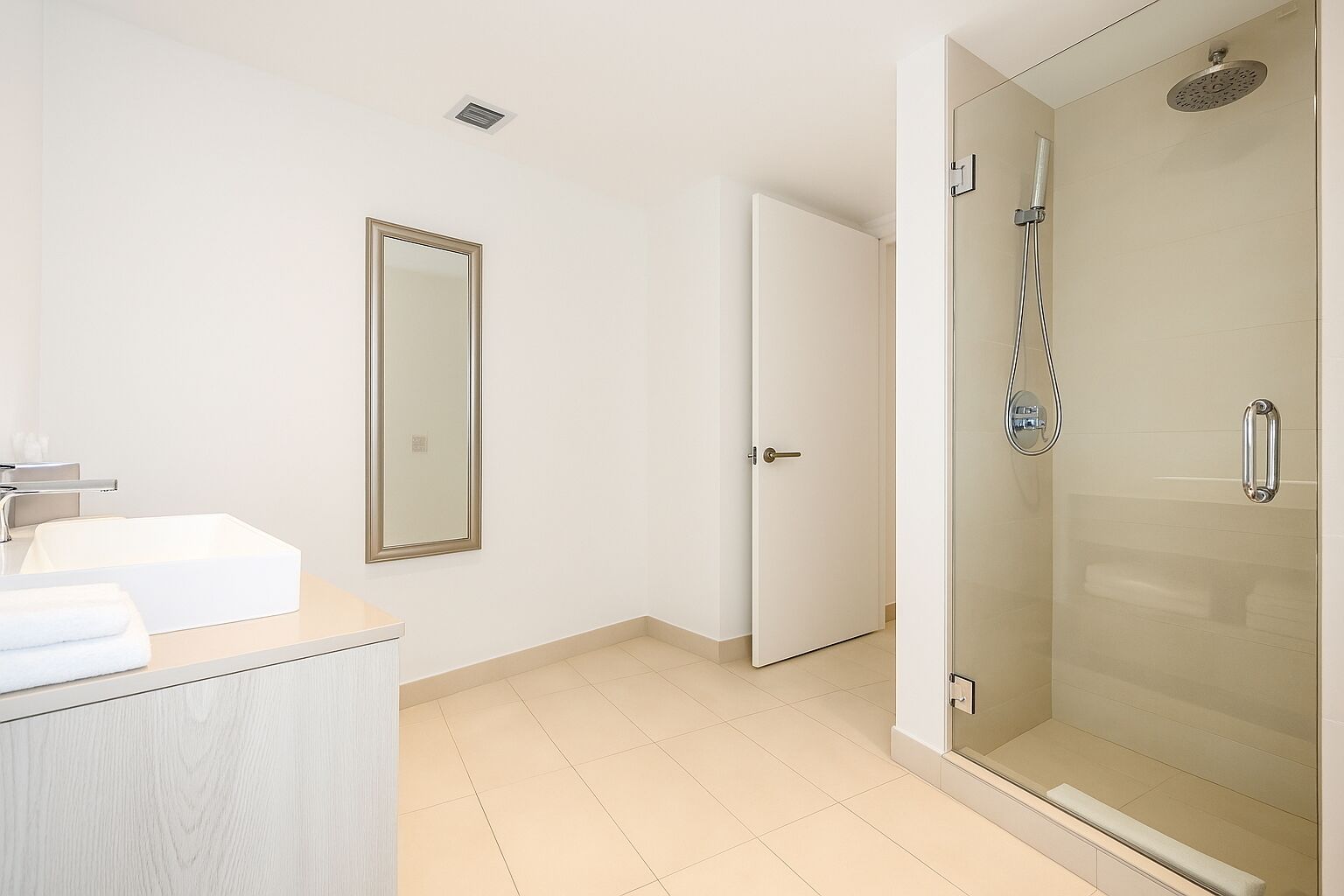 A modern bathroom with a glass-enclosed shower, a large mirror, and a white sink.