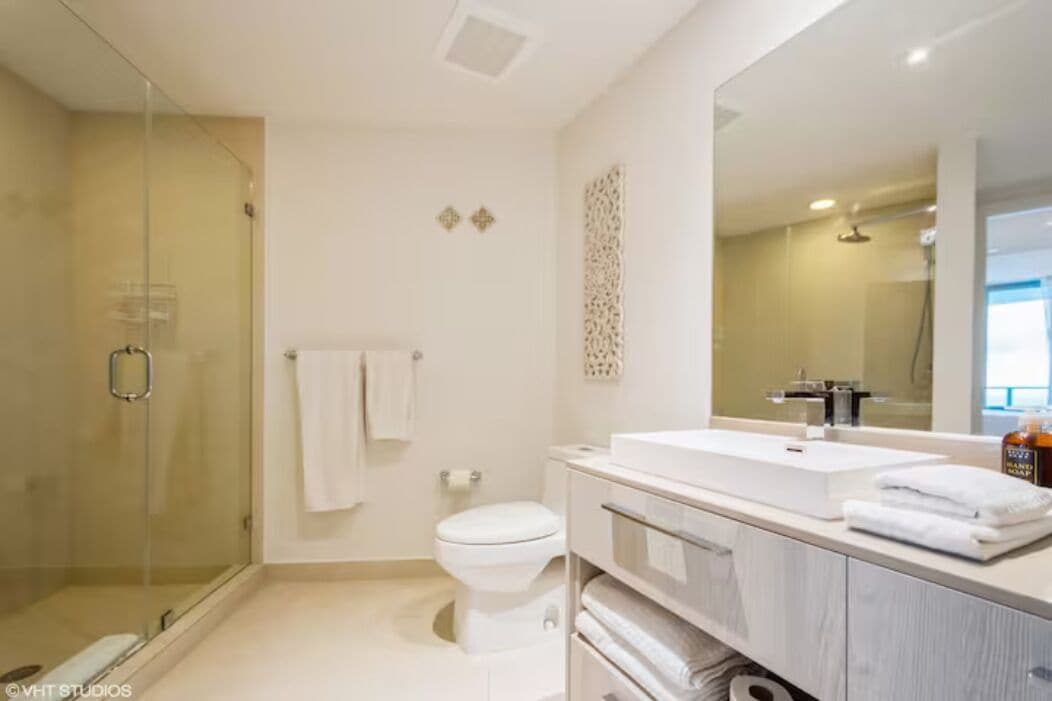 A modern bathroom with a glass shower enclosure, a white toilet, and a vanity with a large mirror.