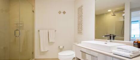 A modern bathroom with a glass shower enclosure, a white toilet, and a vanity with a large mirror.