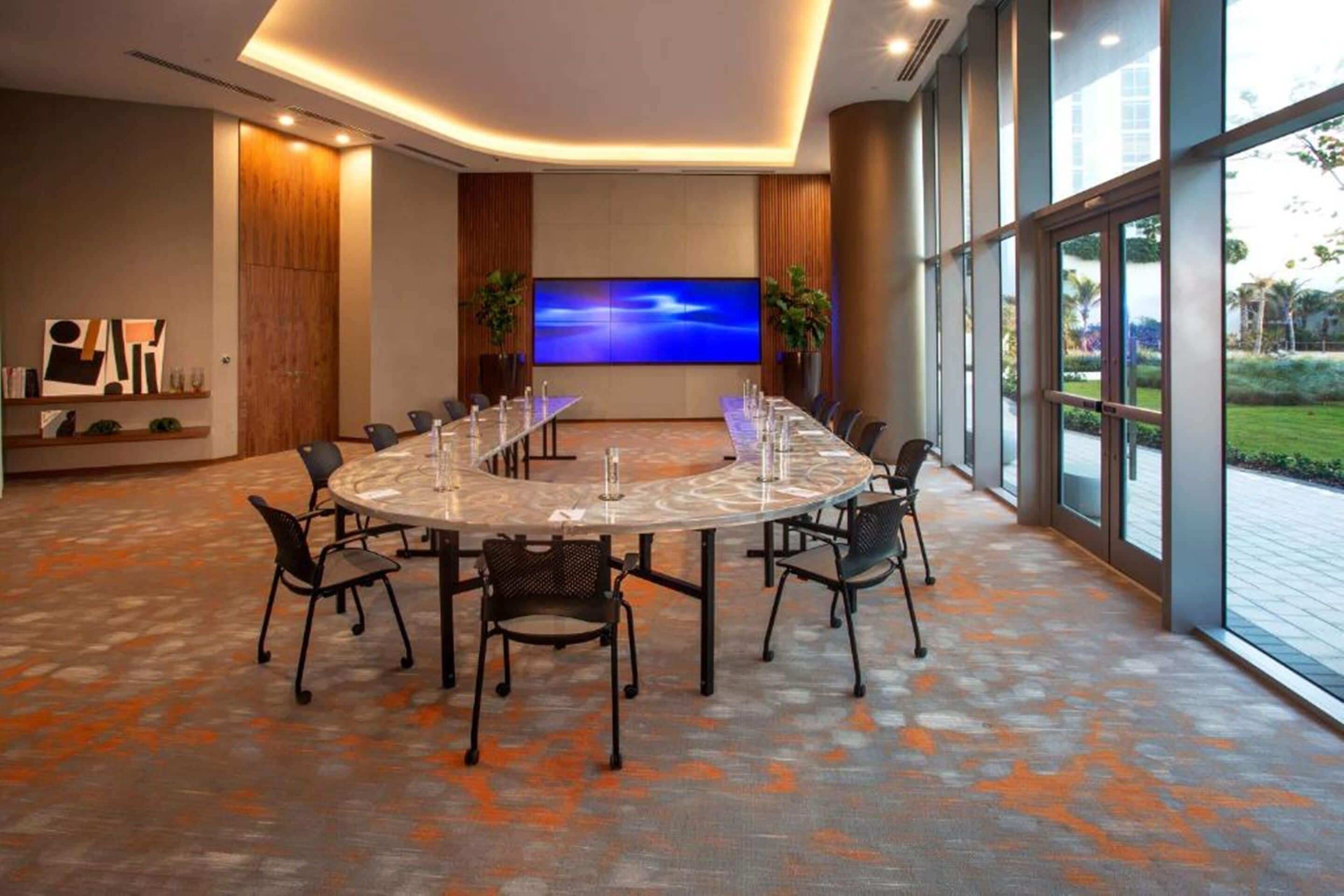 Une salle de conférence dotée d’une grande table ovale, de chaises noires, d’un téléviseur à écran plat et offrant une vue sur l’extérieur grâce à de grandes fenêtres.
