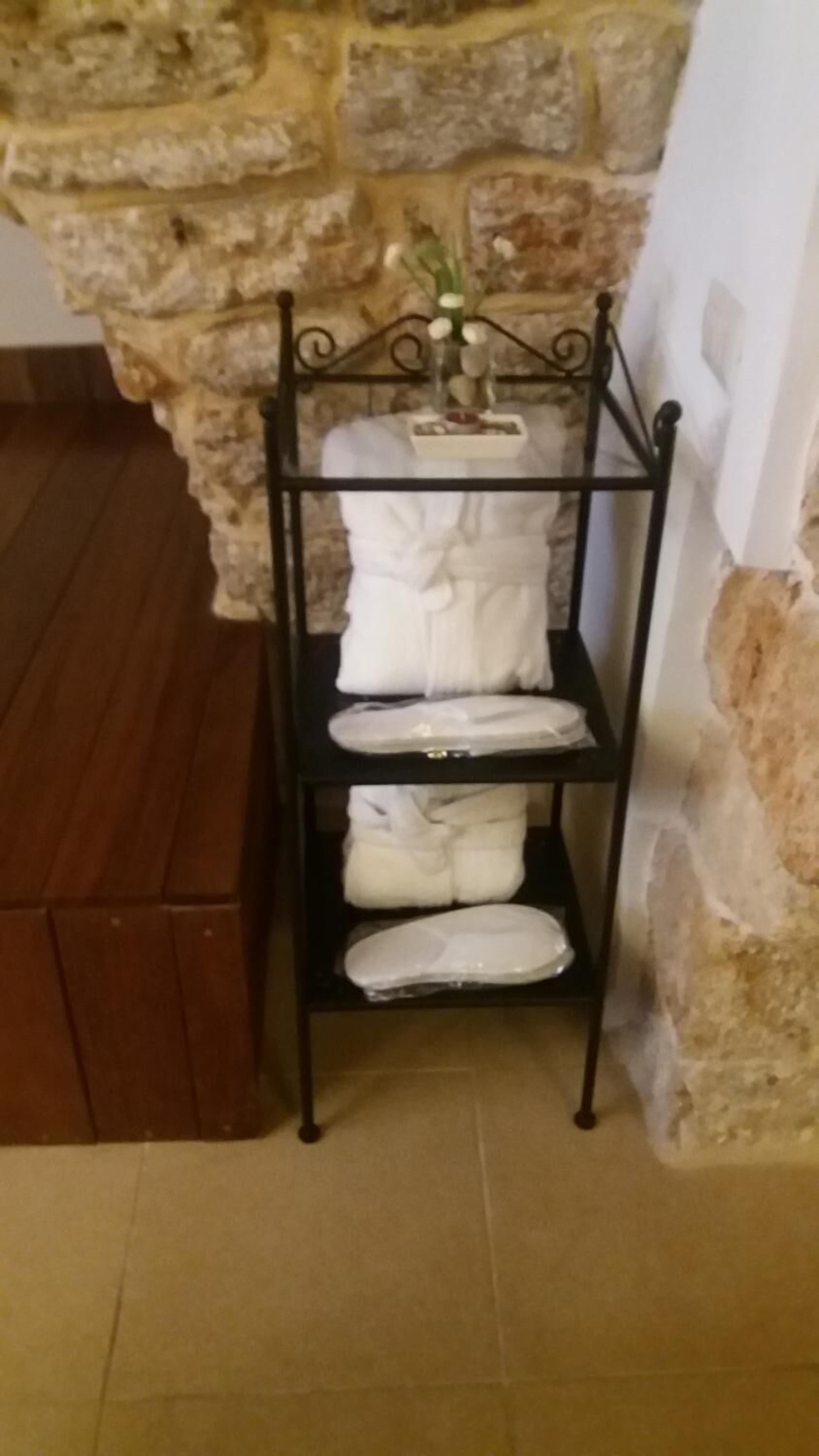 Une étagère en métal noir, sur laquelle sont pliées des serviettes blanches, est adossée à un mur en pierre.