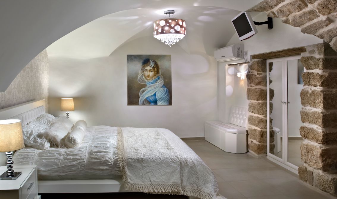 Un dormitorio con cama, un cuadro, una araña y paredes de piedra.