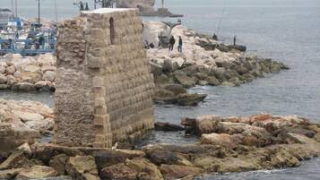 Une structure en pierre située près d’une côte rocheuse, avec des bateaux en arrière-plan.