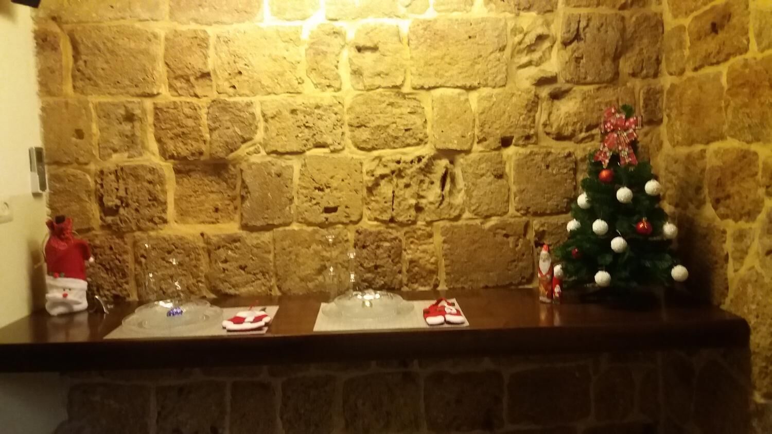 A stone wall with a small Christmas tree and a bottle of wine on a wooden counter.