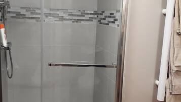 A glass-enclosed shower with a handheld showerhead, a towel rack with towels, and a small mat on the floor.
