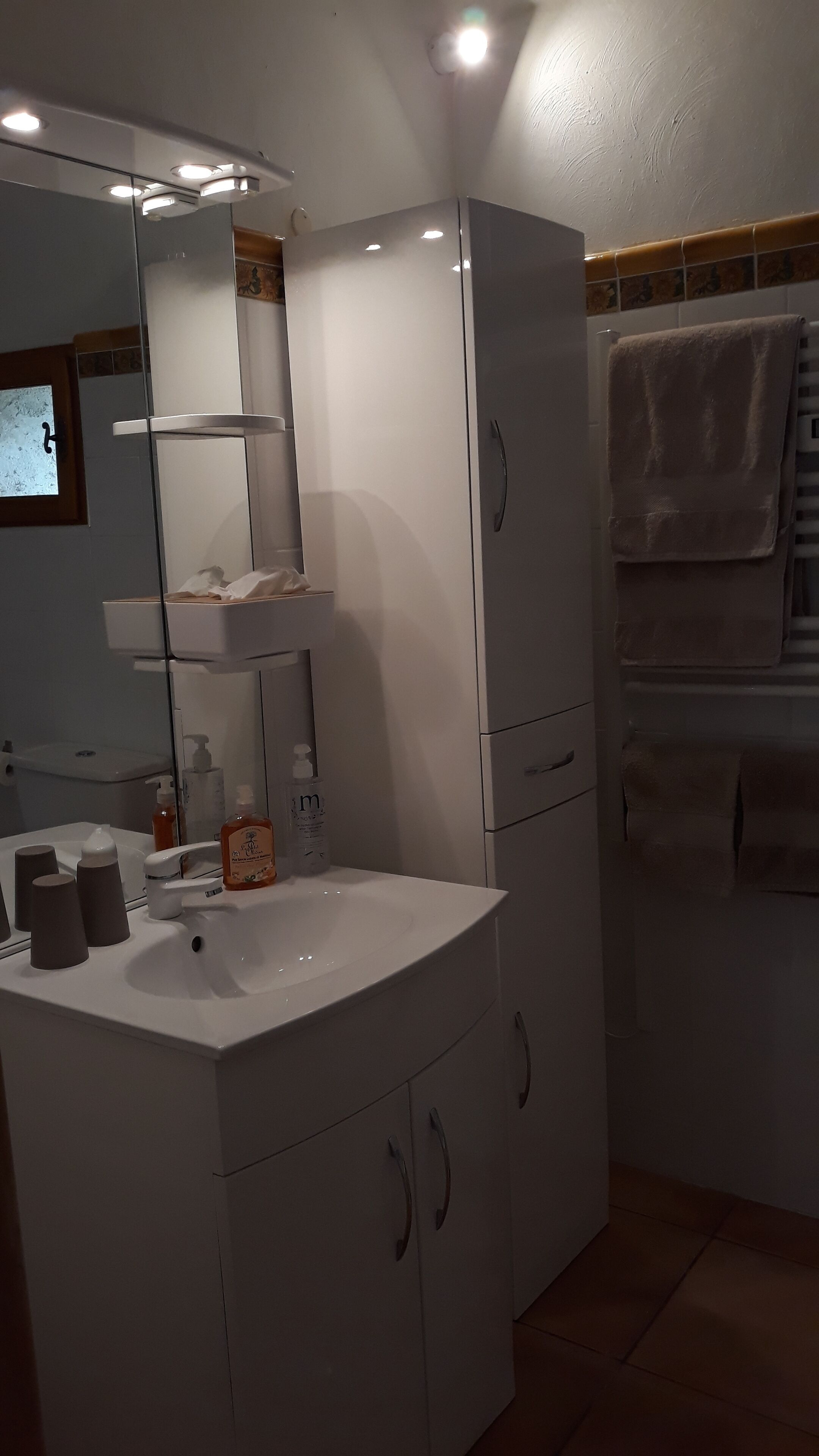 Een moderne badkamer met een wit wastafelmeubilair, een spiegel en een handdoekrek.