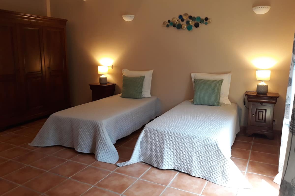 Une chambre avec deux lits simples, chacun doté d’une table de chevet et d’une lampe. La chambre comprend une armoire en bois et un élément décoratif mural.