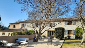 Un bâtiment traditionnel en pierre, doté d’un toit en tuiles, d’un espace extérieur aménagé pour s’asseoir et d’une cour intérieure recouverte de gravier.