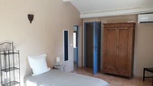Une chambre à coucher comprenant un lit, une armoire en bois, une étagère en métal et une petite table avec une lampe.