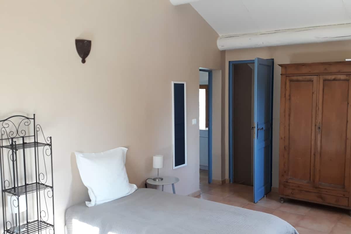 Une chambre à coucher comprenant un lit, une armoire en bois, une étagère en métal et une petite table avec une lampe.
