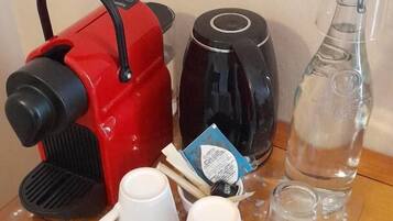 Une table en bois sur laquelle se trouvent une bouilloire électrique rouge et noire, une théière noire, une bouteille en verre transparent et deux tasses blanches.