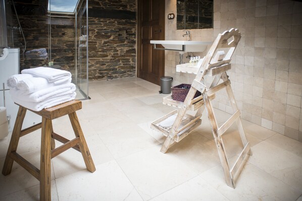 Un baño con un taburete de madera, cabina de ducha con mampara de cristal, lavabo y espejo.