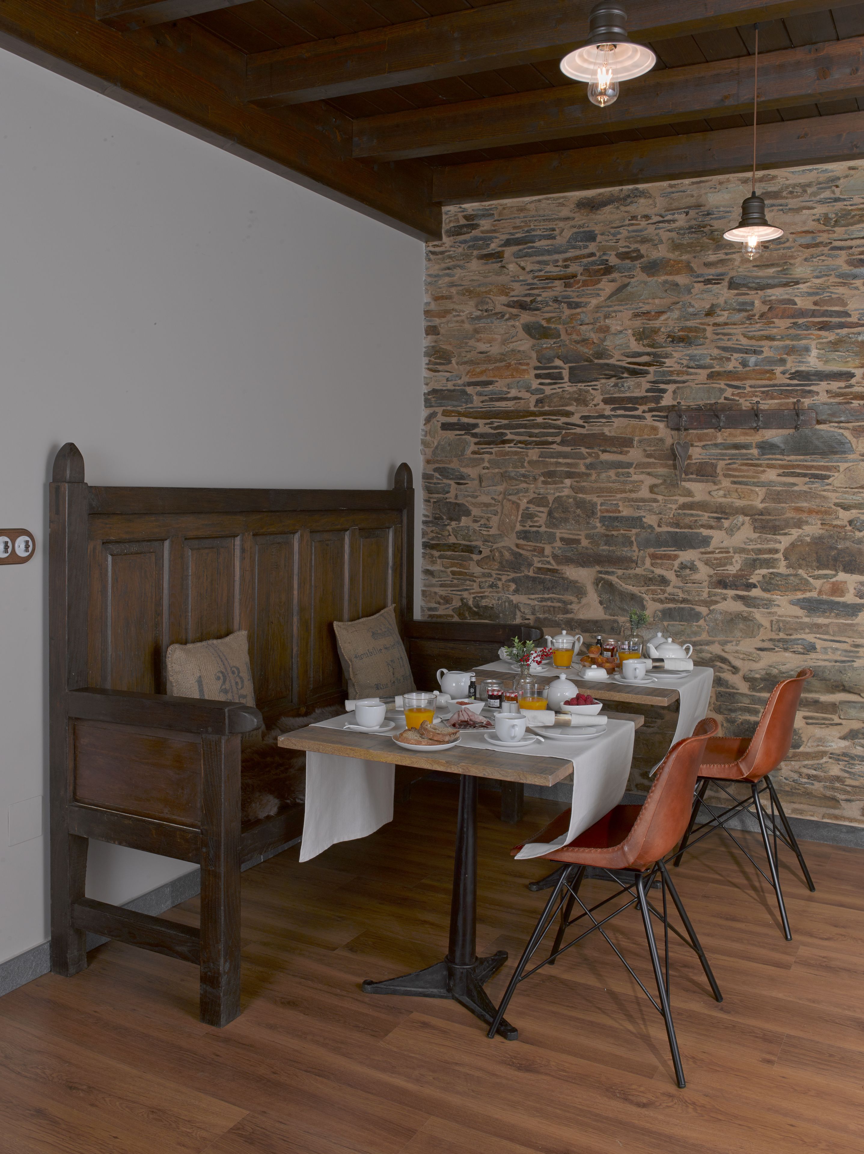 Uma área de jantar rústica com parede de pedra, banco de madeira e mesa posta para o café da manhã.