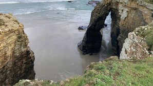 Un paisaje costero con una formación rocosa prominente en arco sobre la playa.