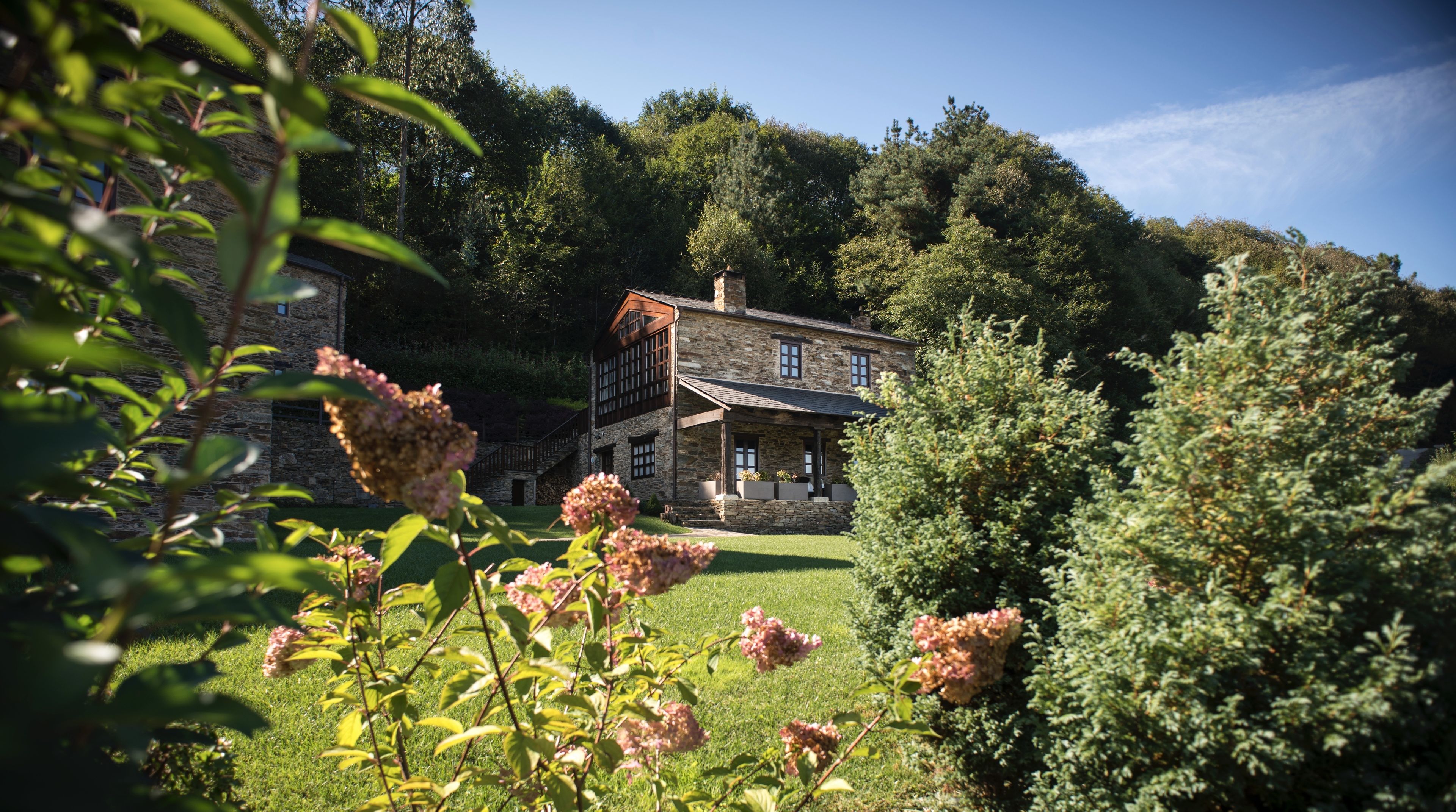 A stone house with a large front porch, surrounded by lush greenery and trees.