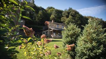 A stone house with a large front porch, surrounded by lush greenery and trees.