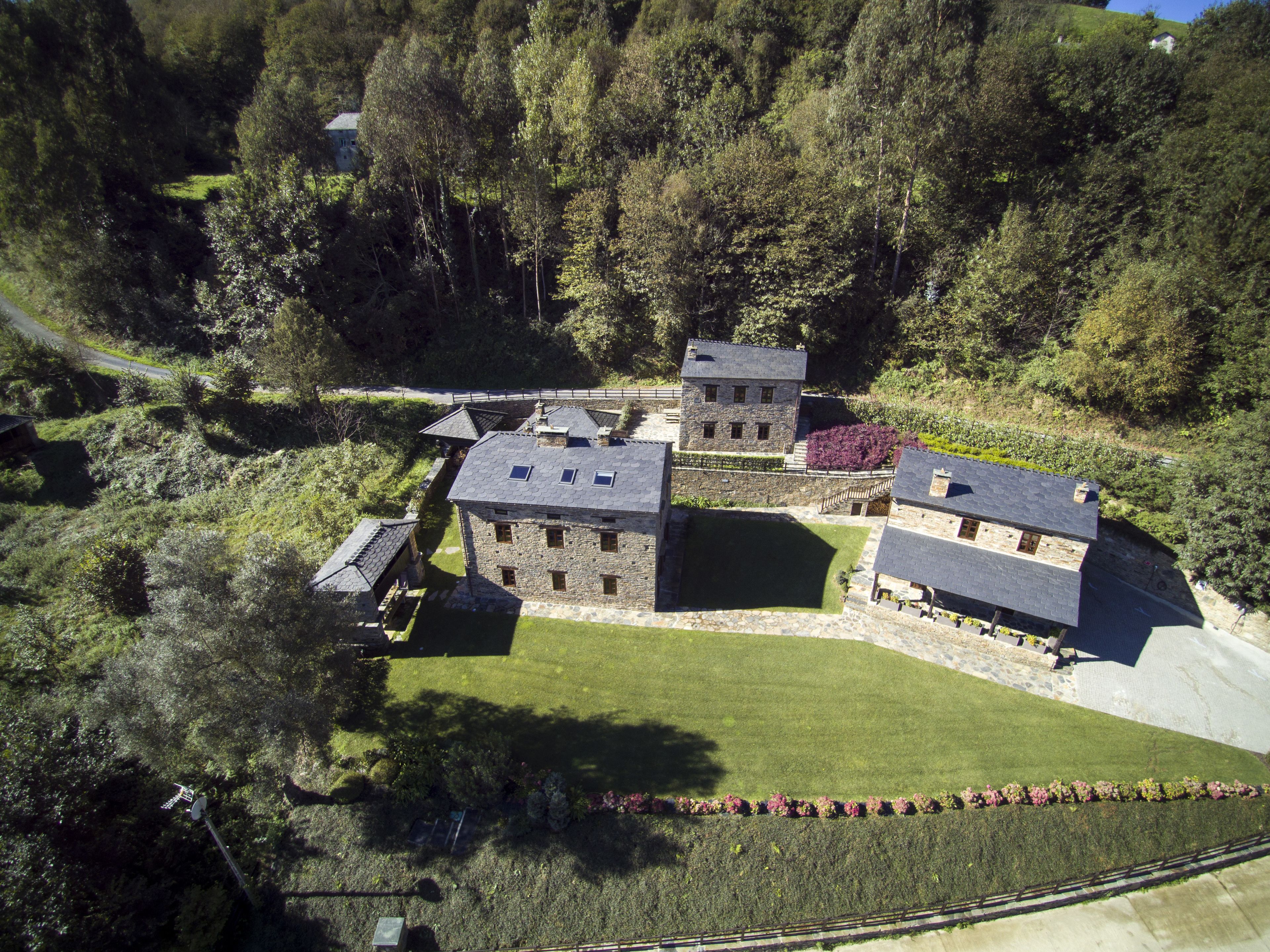 Une vue aérienne d’un ensemble de bâtiments en pierre, entouré d’une végétation luxuriante et d’une pelouse bien entretenue.