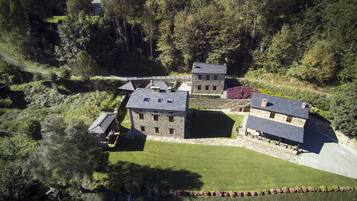 Une vue aérienne d’un ensemble de bâtiments en pierre, entouré d’une végétation luxuriante et d’une pelouse bien entretenue.