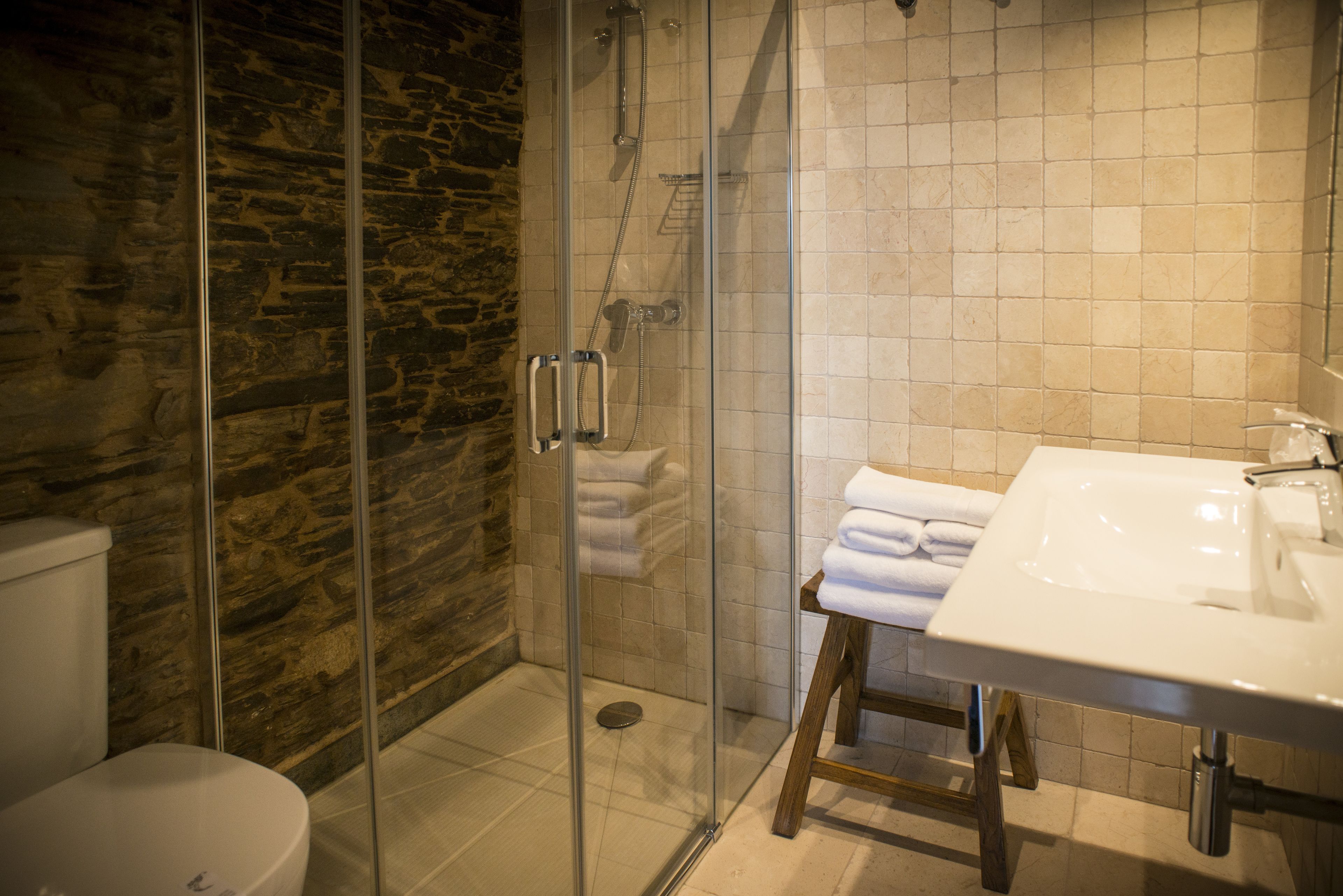 A bathroom with a glass-enclosed shower, a white sink, and a wooden stool.