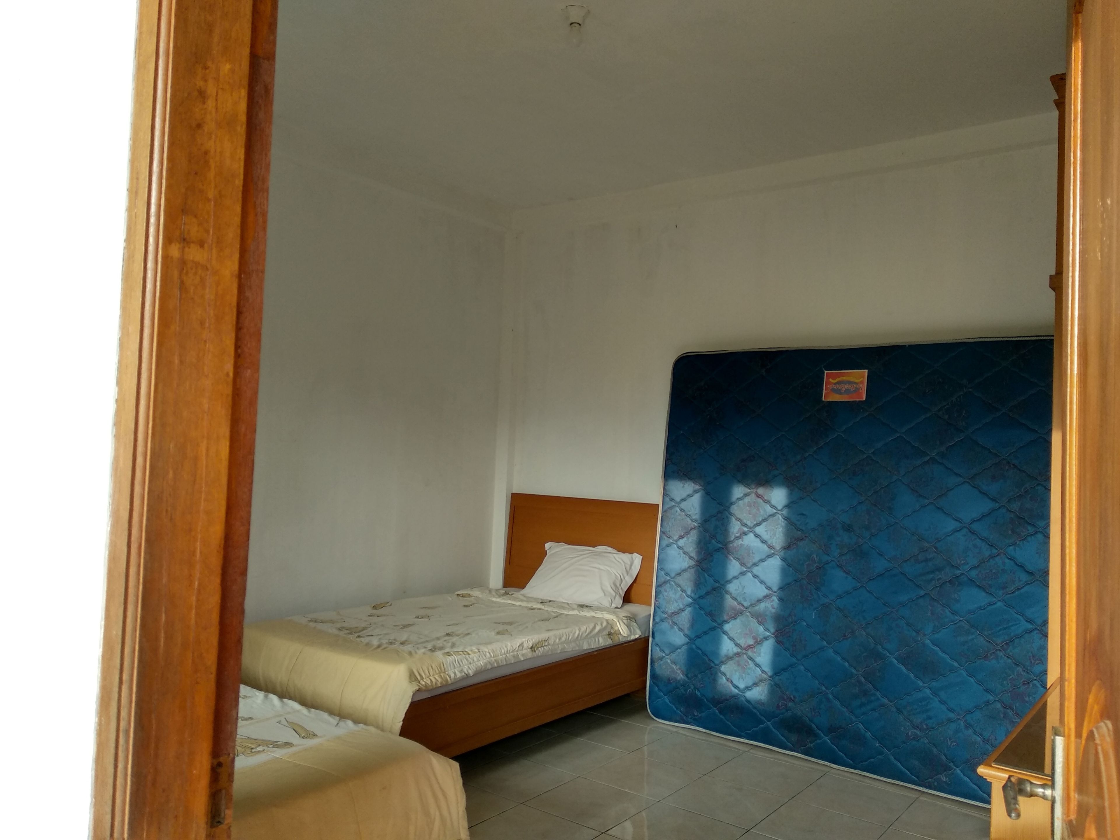 A small, clean room with two single beds, a blue mattress cover, and a wooden headboard.