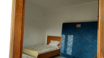 A small, clean room with two single beds, a blue mattress cover, and a wooden headboard.