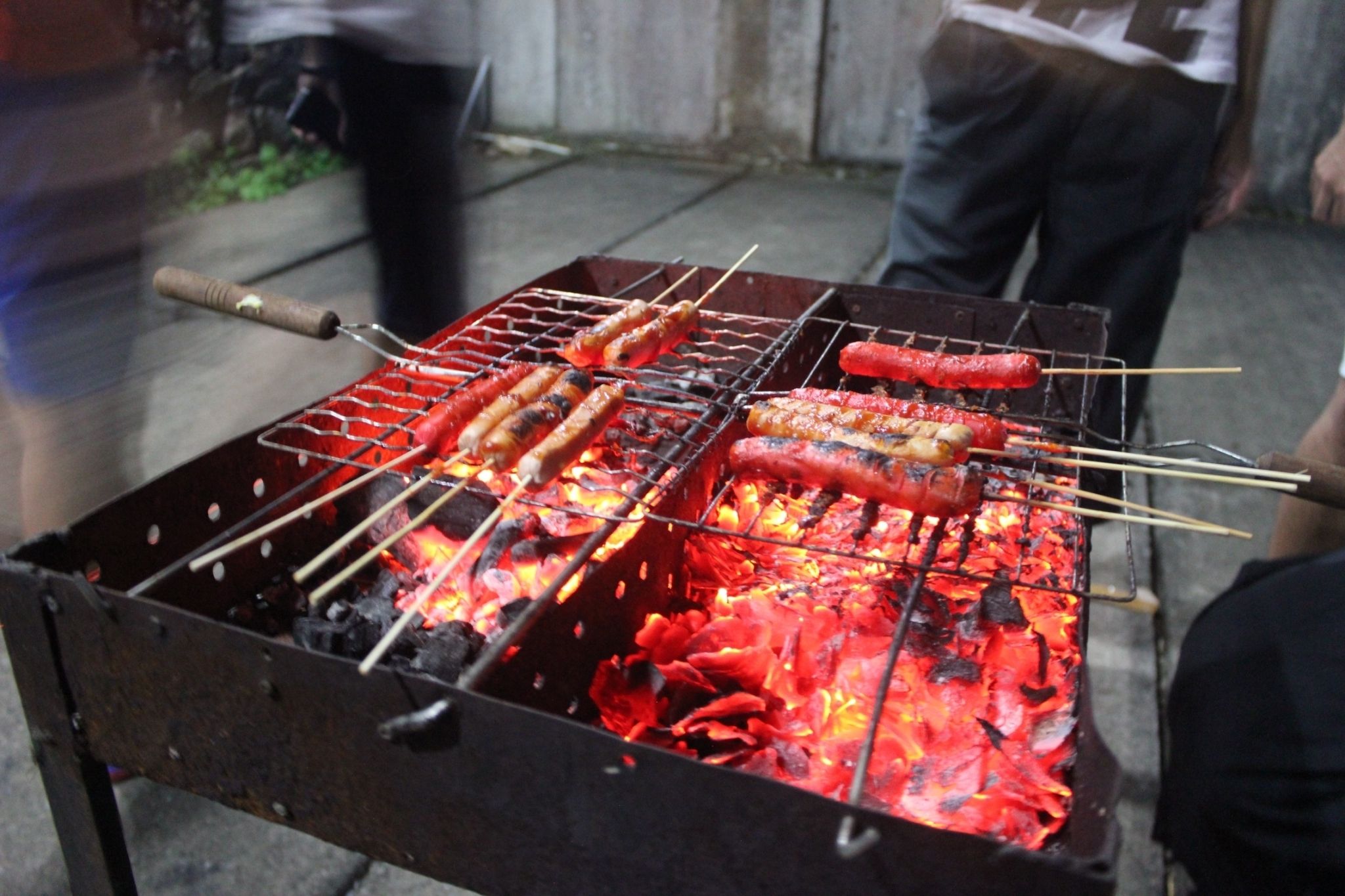 A barbecue grill with skewers of sausages and other meats being cooked over an open flame.