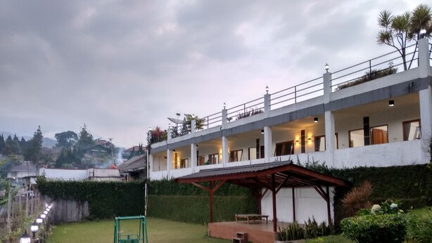 A multi-story building with a covered patio area, a small garden with a swing set, and a pathway leading to the entrance. - The View Villa (Cisarua)