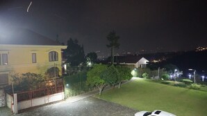 A residential area at night with a well-lit house, a gated driveway, and a lawn. - The View Villa (Cisarua)